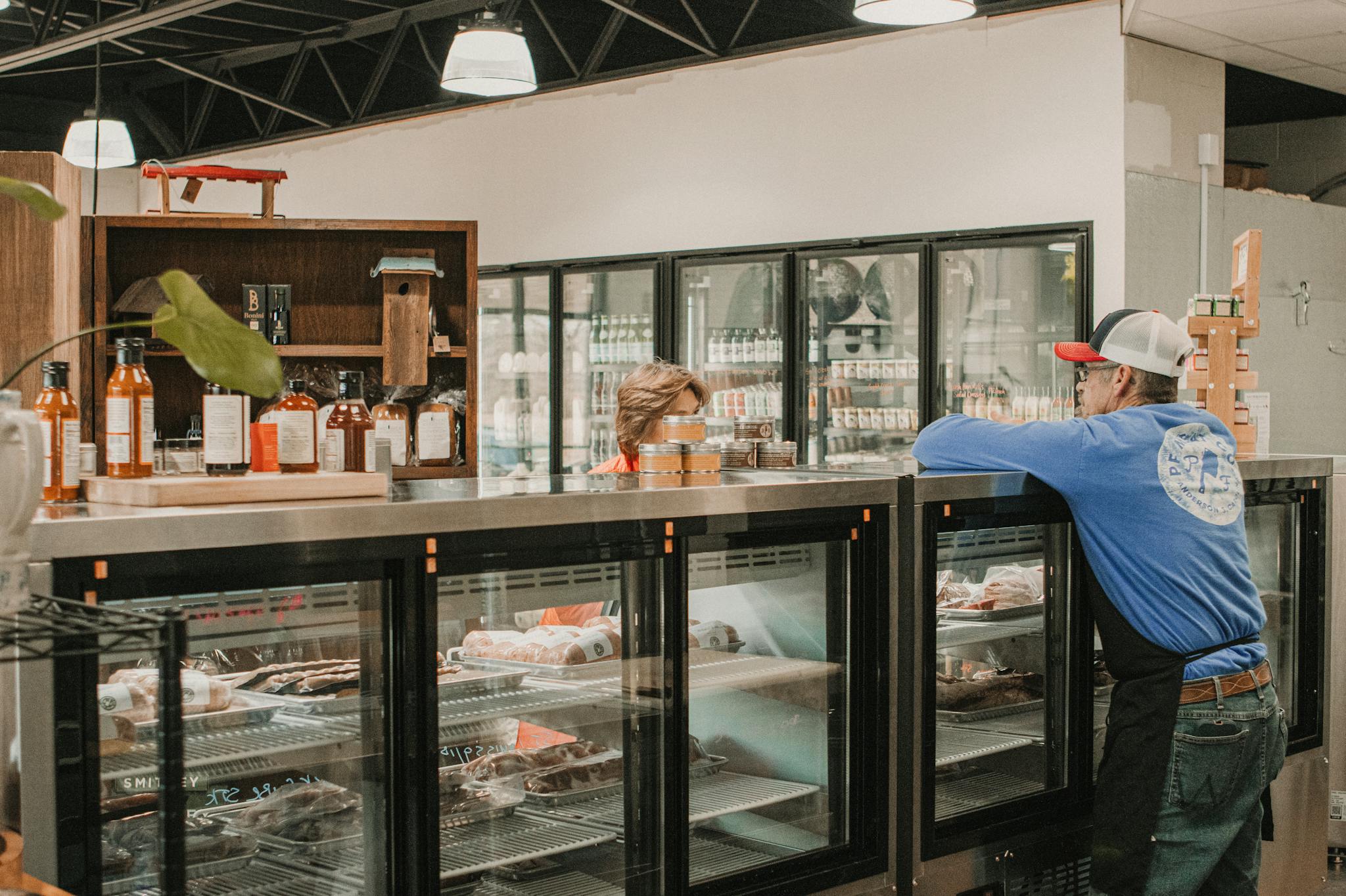 A butcher serving a customer at a local store with fresh meats on display.
